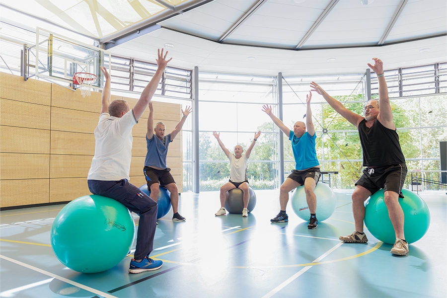 Ein Therapeut leitet mehrere Patienten bei einer Übung auf dem Gymnastikball an.